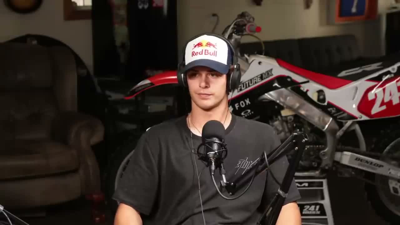 A guest on a close-up camera in front of a race bike, speaking into a studio microphone