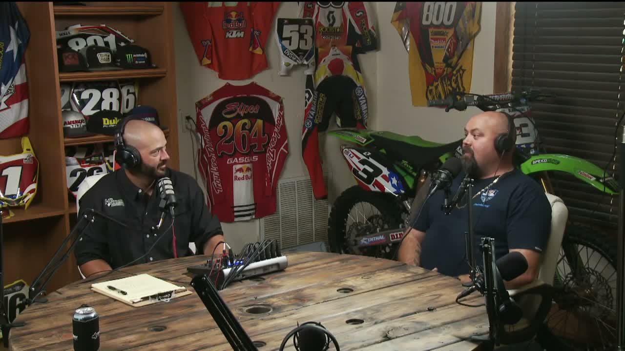 Two hosts at the round wooden table in The Legends Room, with signed race jerseys behind them